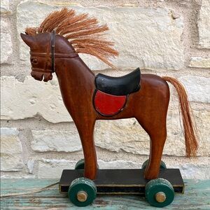 Vintage hand-carved wooden pull toy horse mounted on a wheeled platform.